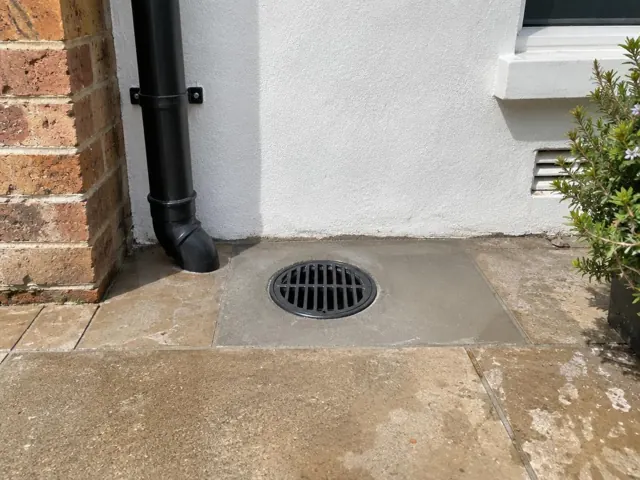 Outdoor drain grate set in dry paved courtyard beside a wall in Bondi