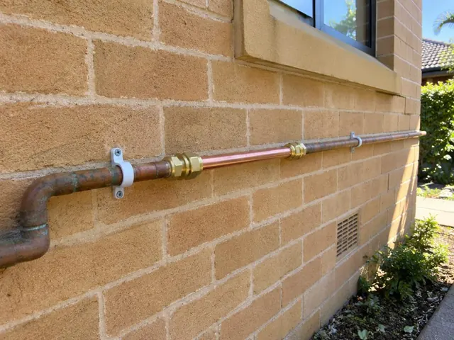 Repaired copper water pipe running along a brick exterior wall beside a window in Vaucluse