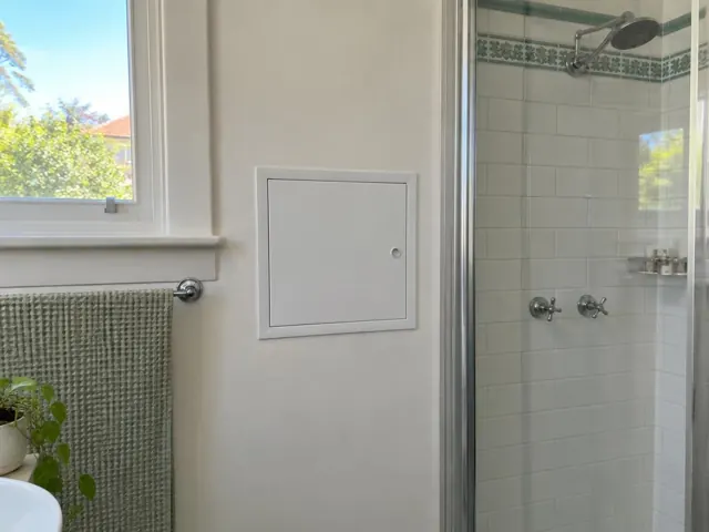 Small wall access panel beside a tiled shower in a bathroom with a window and towel rail in Vaucluse